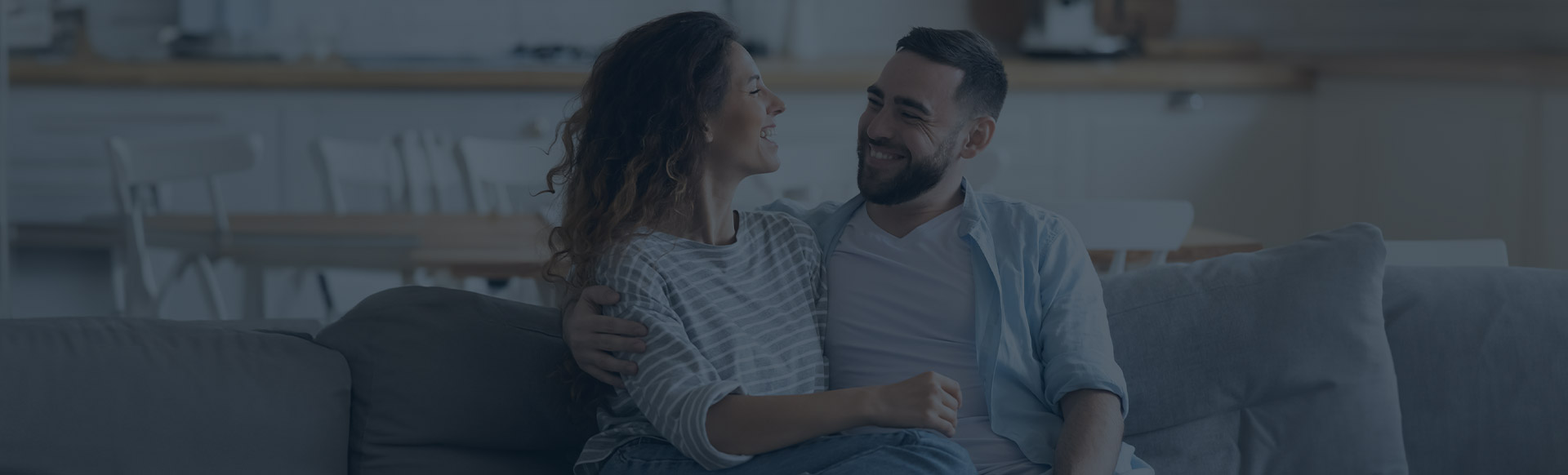 A couple smiles at each other sitting on a couch